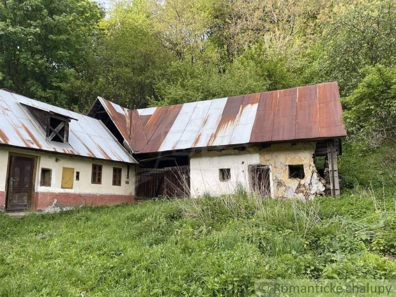 An older family house in Hačava, surrounded by greenery and trees, with rusty roofs.