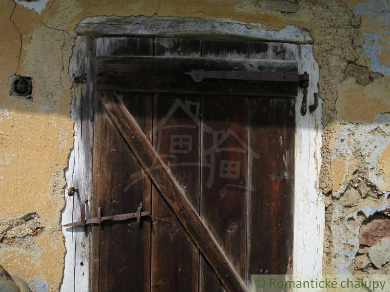 Worn wooden door in a family house in Hačava, set in peeling plaster.