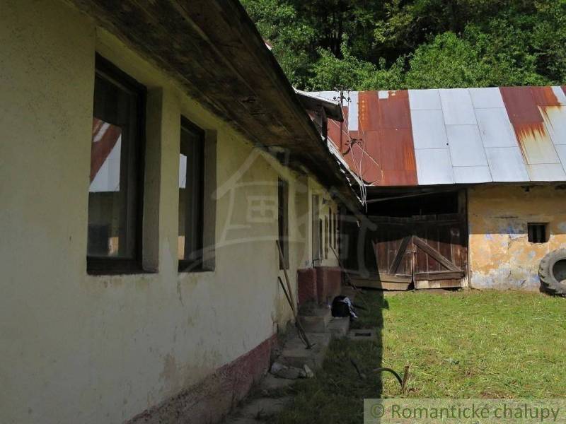 A family house in Hačava with a garden, a wooden fence, and a metal roof surrounded by nature.