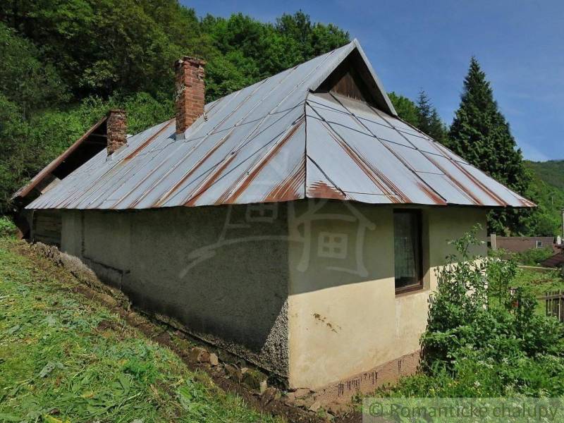 A family house in Hačava with a metal roof, situated near a forest and a green meadow.