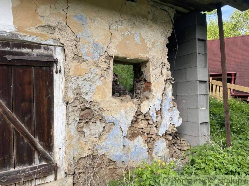 A weathered wall of a family house in Hačava with wooden doors and damaged plaster.
