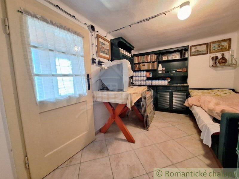 The interior of a cottage with cream-colored doors, a table, and a sofa, a shelf with books and decorations.