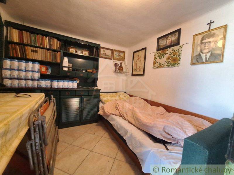 A room in a cottage with a bed, a bookshelf, and paintings on the wall.