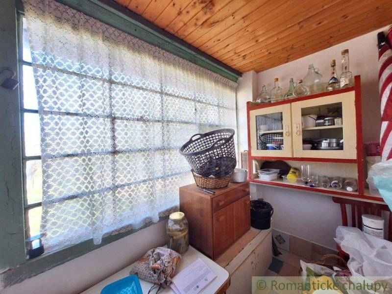 The interior of a cottage with a wooden ceiling, cabinets, and a basket on the window with a curtain.