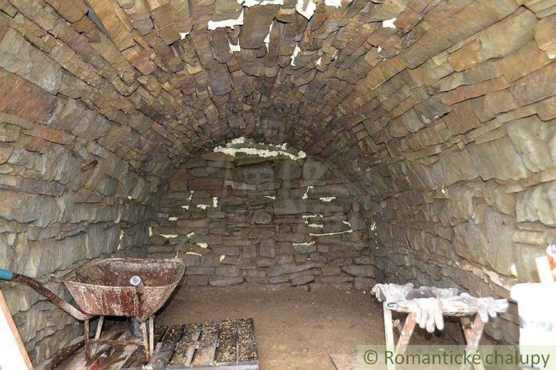 Stone vaulted cellar space with a wheelbarrow and wooden pallets in the gardens.