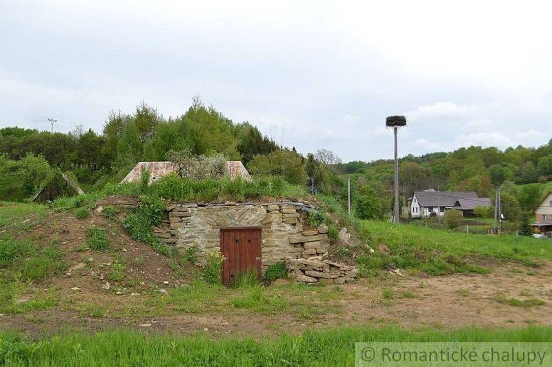 Stone cellar with a green roof in the Gardens in Kečkovce and rural houses in the background.