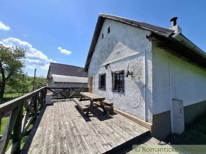 Cottage in Podkriváni with a wooden terrace and a bench under the blue sky.