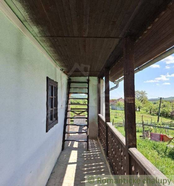 A wooden terrace with stairs at the cottage in Podkriváň offers a view of the surrounding countryside.