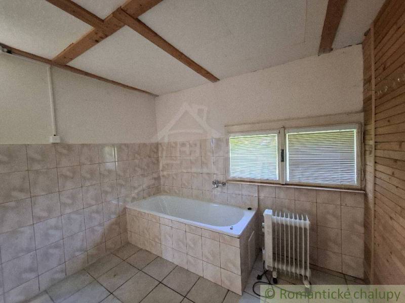 A bathroom in a cabin with a bathtub and a radiator, tiled with a view from the window.