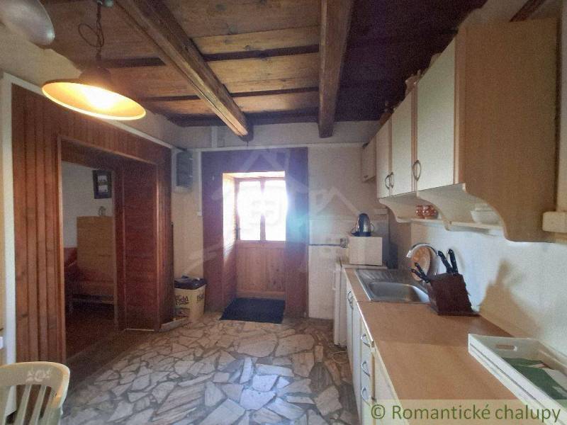 A kitchen in a cottage with a wooden ceiling and stone floor, warm lighting.