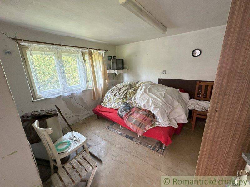 A room in a family house with a bed, a chair, and cracks on the wall.