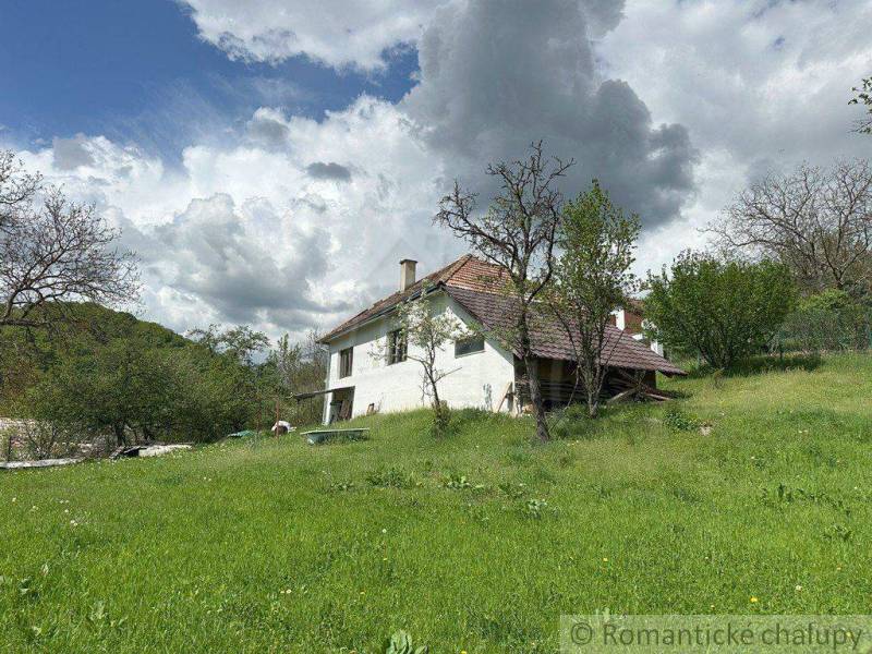 A family house in Kokava nad Rimavicou surrounded by greenery and old trees under a sky with clouds.