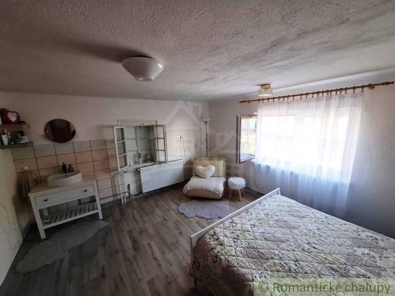 A bright room in a family house with a bed, a sink, a chair, and a large window.