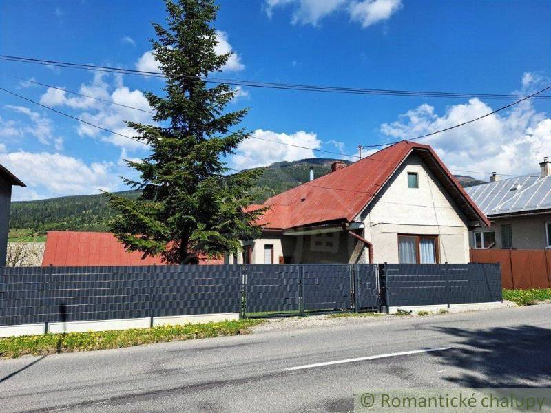A family house in Telgárt with a red roof, a tall tree, a fence, and a road.