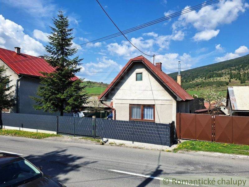 A family house in Telgárt with a red roof, a fence, trees, and hills in the background.
