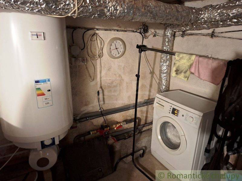 Laundry room in a family house with a washing machine, boiler, and pipes.