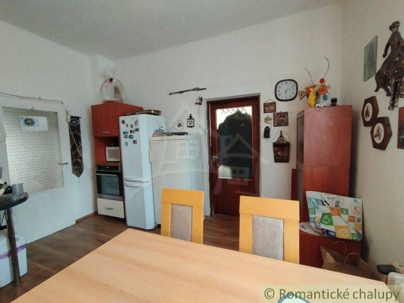 Dining room with a wooden table, kitchen unit, decorations, and accessories in a family house.