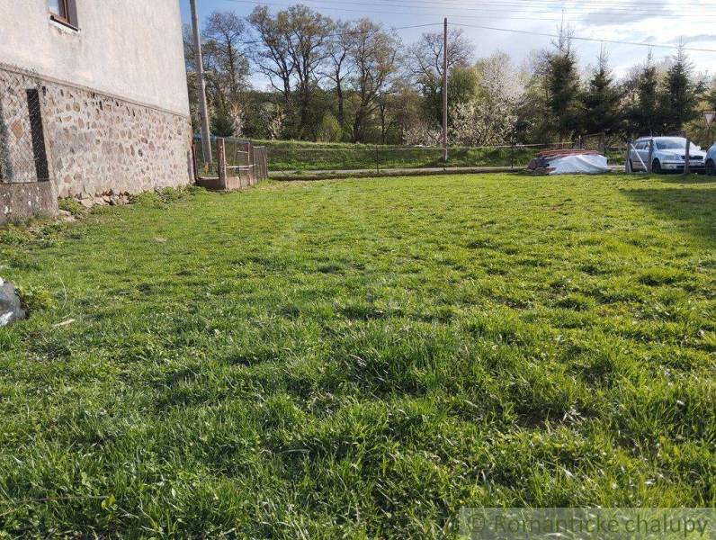 Lawn in front of the family house, parked car next to it, visible stone wall and trees.