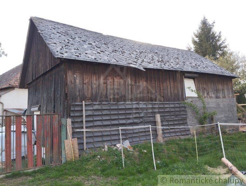A wooden family house with a worn-out roof and fencing on a grassy plot.