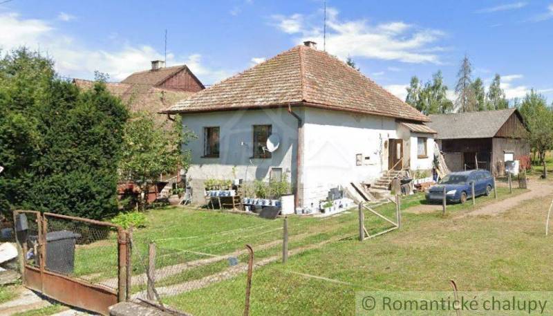 A family house with a traditional roof, a garden with greenery, next to it a farm building, a car.
