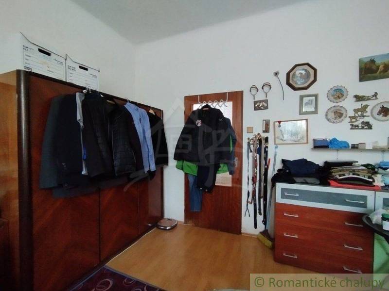 In the room of the family house, there is a wardrobe with jackets, a dresser, and decorations on the wall.