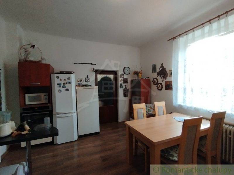 Dining room with table, chairs, and a family house with a kitchen unit, window, and decorations.