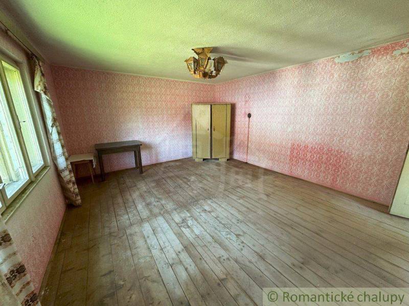In the room of the family house, there is a table, cabinets, wooden floor, and pink wallpaper.