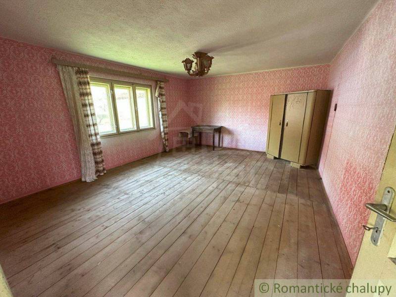 A room with a wooden floor, an antique wardrobe, pink walls, and a table in a family house.