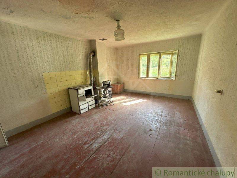 An old family house with a tiled stove, wooden floor, and light through the window.