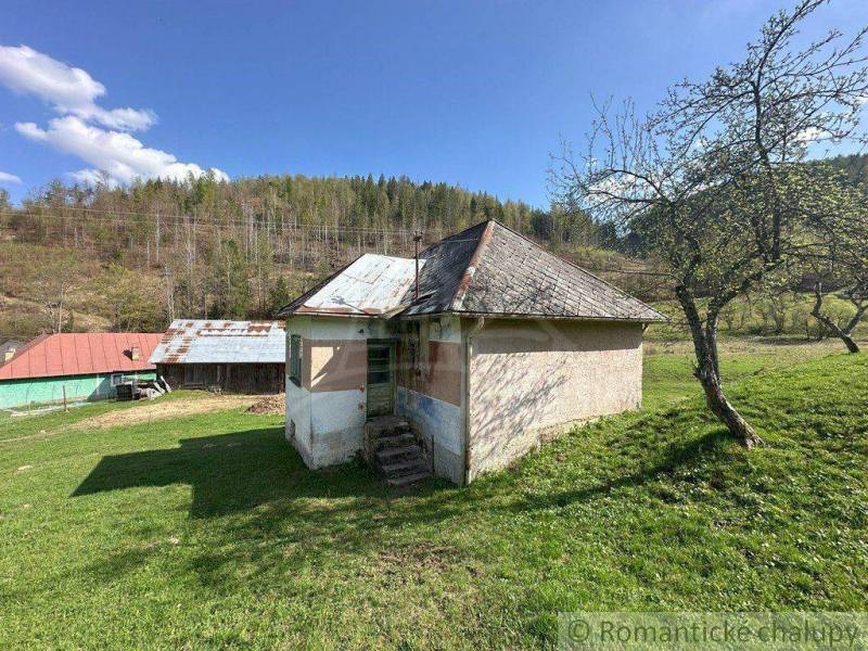An old family house with a wooden roof in the middle of a green landscape and hills.