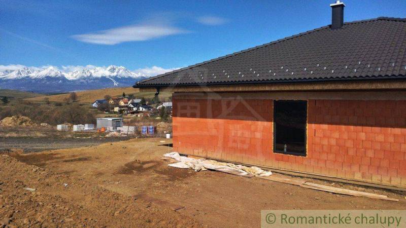 A family house under construction with a view of snow-covered mountains and hills.