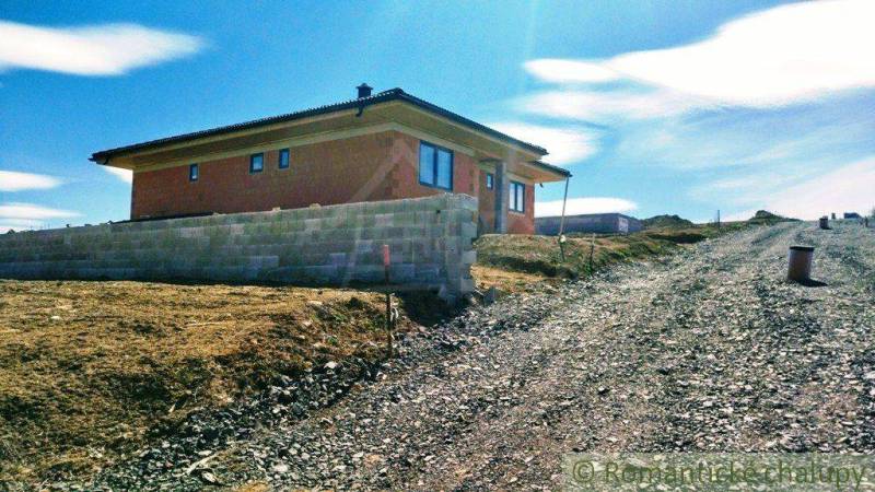 A family house on a slope next to a gravel road is surrounded by a clear blue sky.