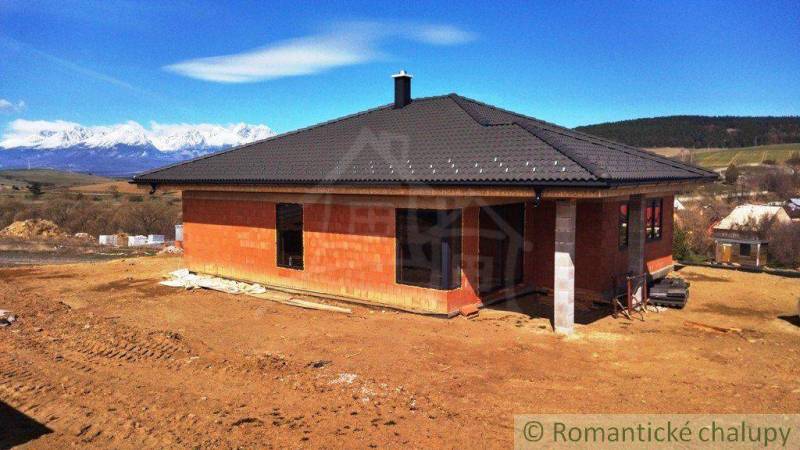 Construction of a family house with a black roof in a picturesque rural setting with mountains.