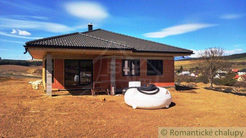 A family house under construction in the countryside, with a sloped roof and open space.