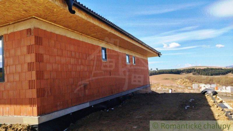 A family house under construction with a brick wall in the countryside, with nature and fields in the background.