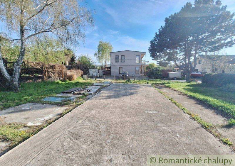 A paved plot with trees and a house in the back, suitable for recreational living.