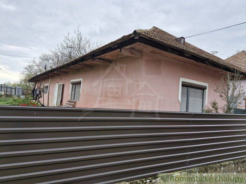 A family house with a metal fence and a satellite dish, with flower beds in the background.