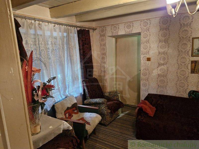 A room in a rustic cottage with a comfortable armchair, floral decorations, and wallpaper.