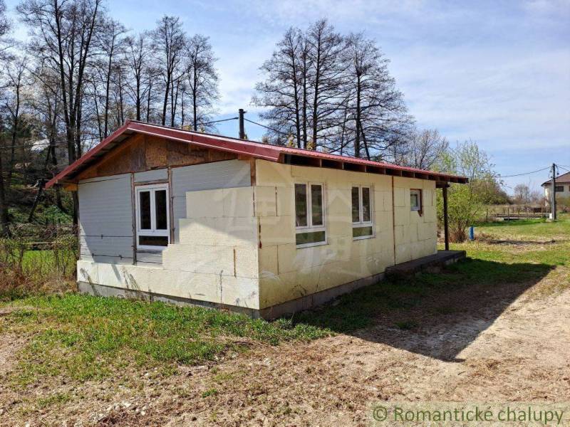 A cottage in nature with a white facade surrounded by grass and trees, an ideal place to relax.