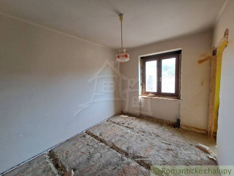 A room in a family house with an unfinished floor, one window, and a hanging light fixture.