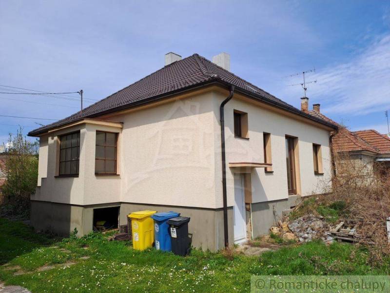 A family house with two ground-floor windows, a lawn, and waste containers in the yard.