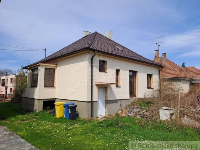 A family house with a brown roof, next to a green lawn and flowers in front of the garden.
