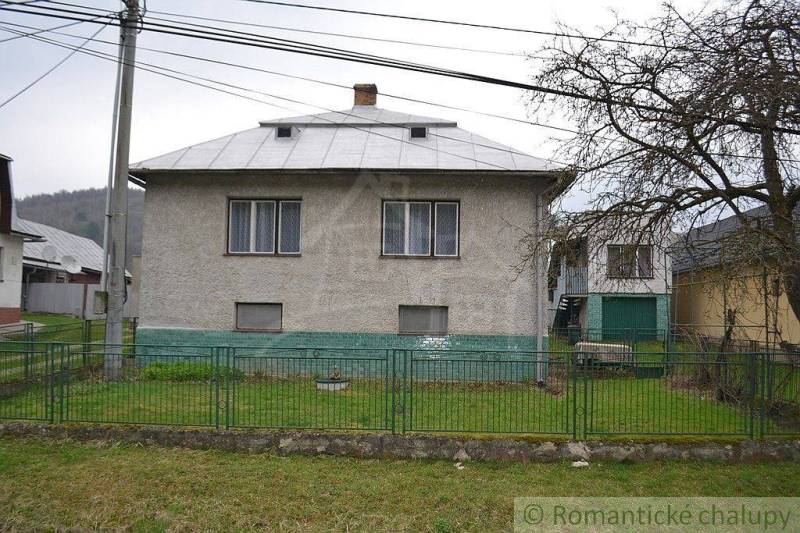 A family house with a white metal fence and green lawn, next to an old tree.