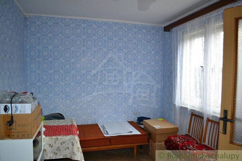 A room with patterned wallpaper, decorated in blue, next to it is a family house.