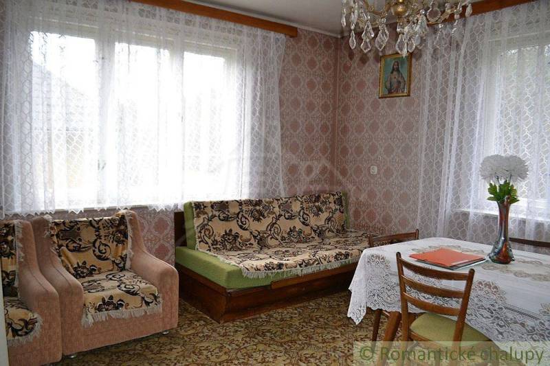Living room of a family house with tapestry upholstery, crocheted curtains, and wall decorations.
