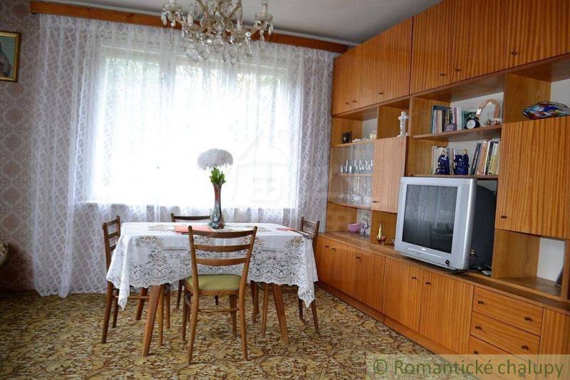 Dining room of a family house with a wooden living room, television, and a lace tablecloth on the table.