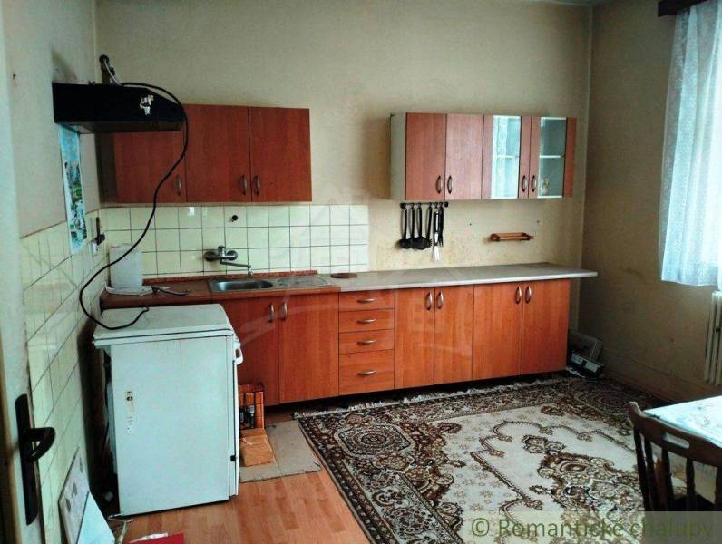 A kitchen in a family house with wooden cabinets, carpet, and a white countertop.