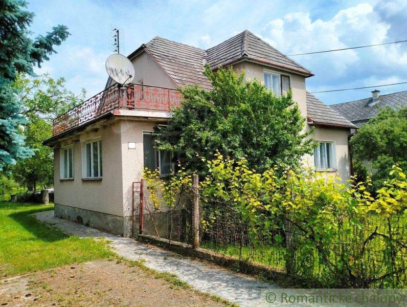 A family house in Košeca with a wooden fence and a garden, surrounded by greenery.