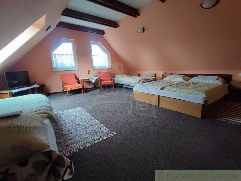 Attic room with five beds, TV, armchairs, and tables in a family house.