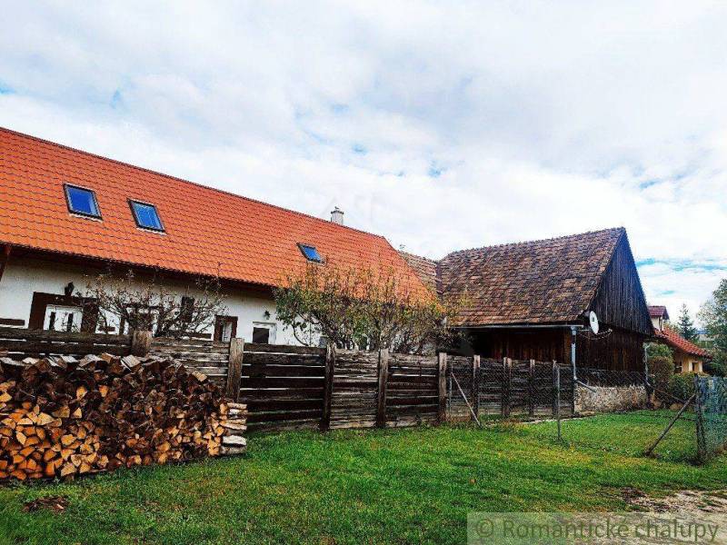 A family house with a wooden fence, a garden, and a pile of wood in the countryside.